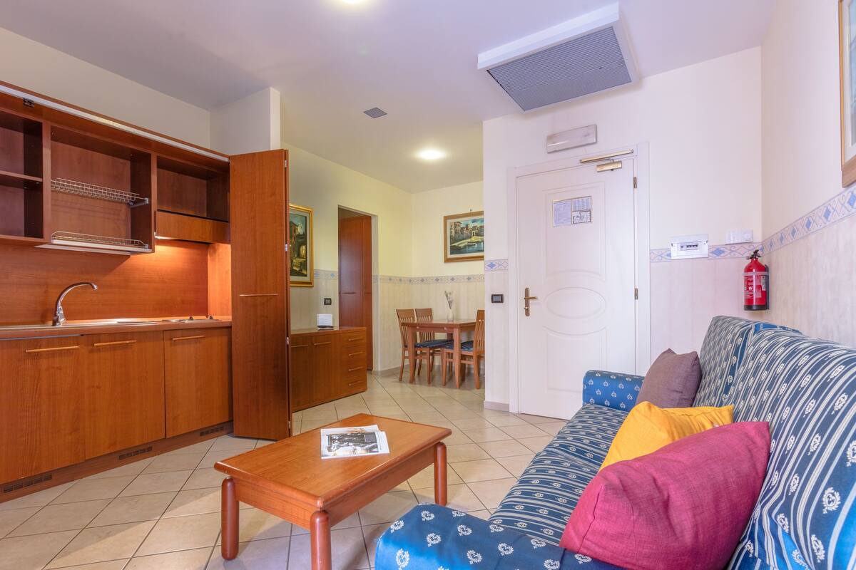 A compact living space with a kitchenette, a dining area, and a sofa with cushions.