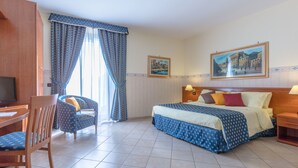 Una habitación de hotel con una cama, un escritorio, una silla y dos cuadros en las paredes.
