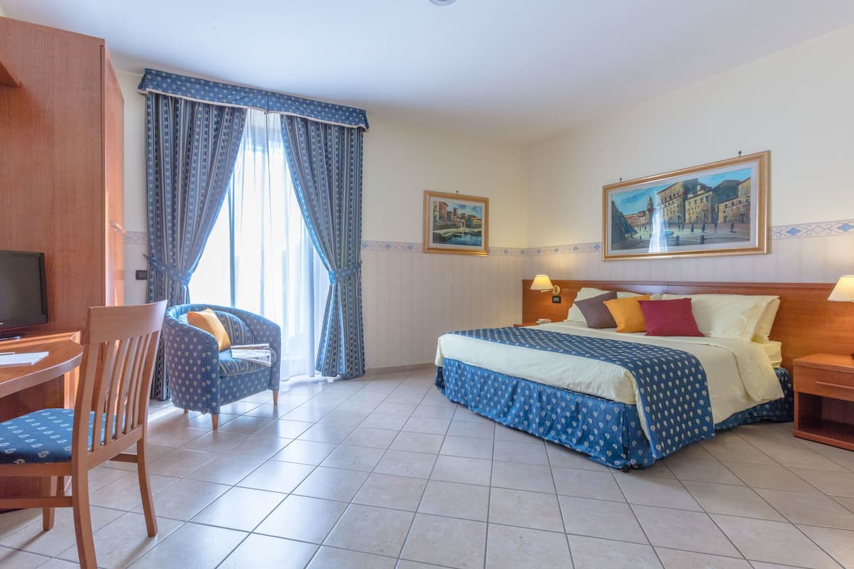 A hotel room with a bed, a desk, a chair, and two paintings on the walls.