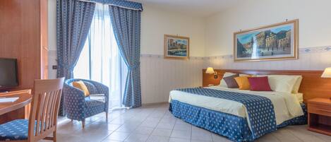 A hotel room with a bed, a desk, a chair, and two paintings on the walls.