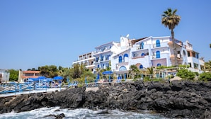 Un hotel sulla costa con diversi balconi, un litorale roccioso e una palma.