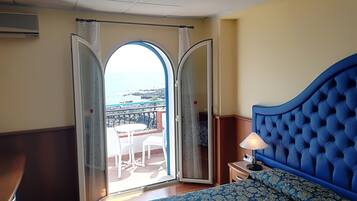 Habitación de hotel con una cama grande, un balcón con vista al mar y una pequeña mesa con sillas.