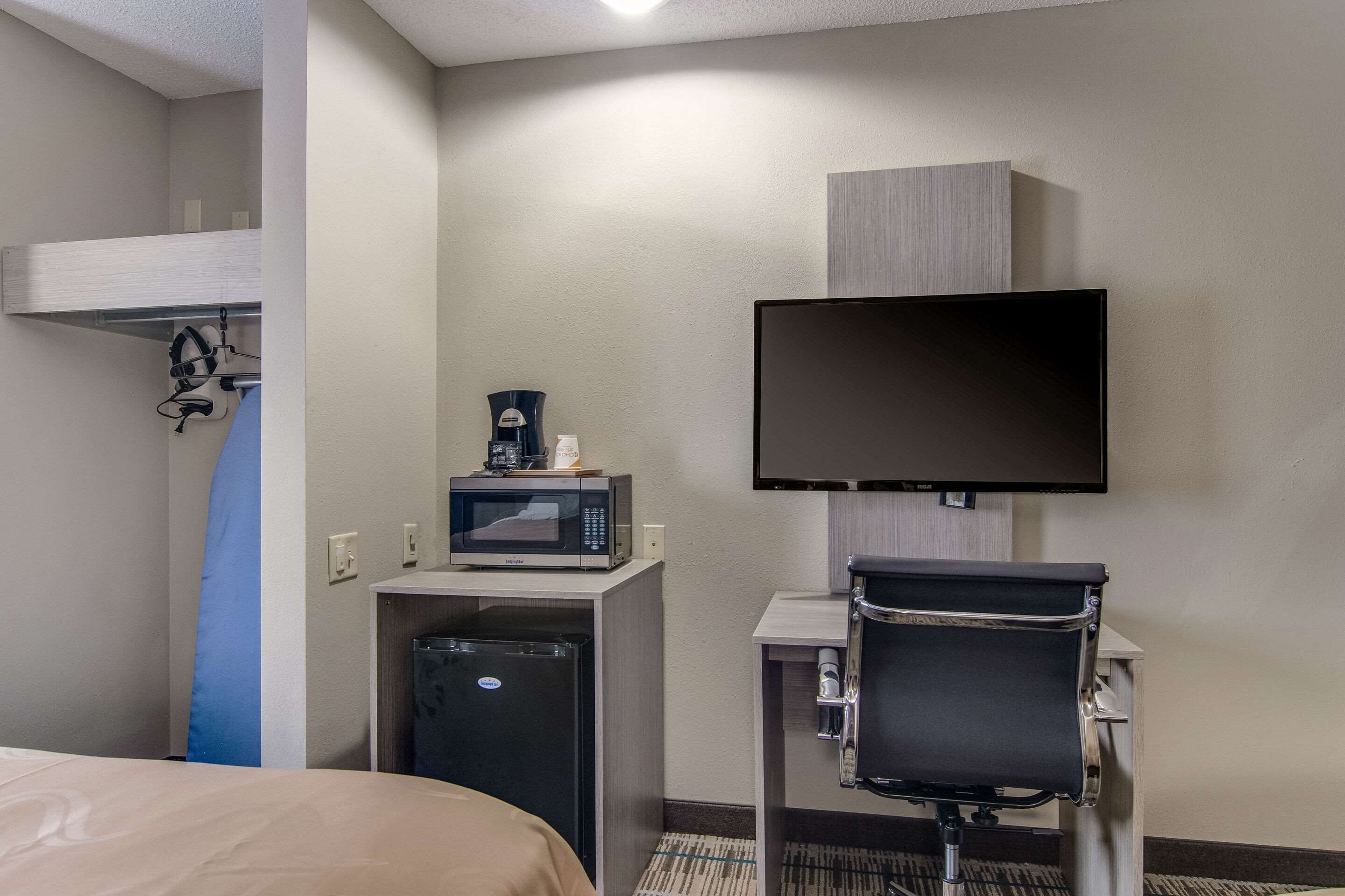 Habitación de hotel con cama, escritorio con silla, microondas, refrigerador, televisor y cafetera.