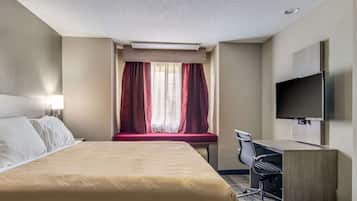 Habitación de hotel con cama, escritorio, silla, televisor y ventana con cortinas.