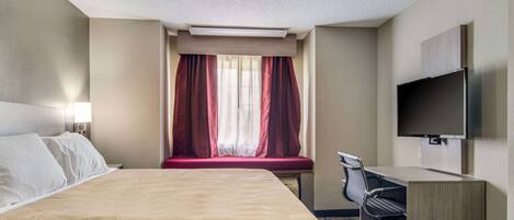 Habitación de hotel con cama, escritorio, silla, televisor y ventana con cortinas.