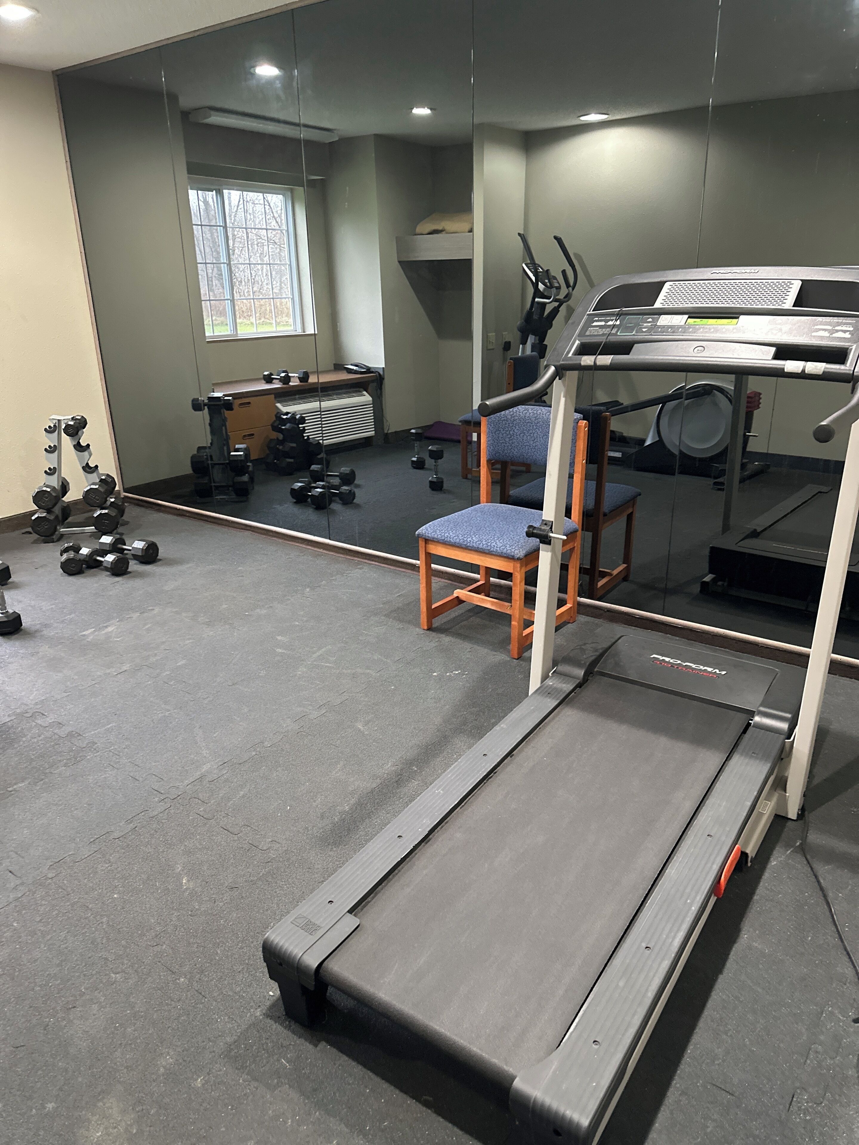 A gym with a treadmill, exercise equipment, and a chair.