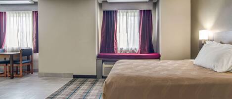 A hotel room with a bed, a desk, and a window with curtains.