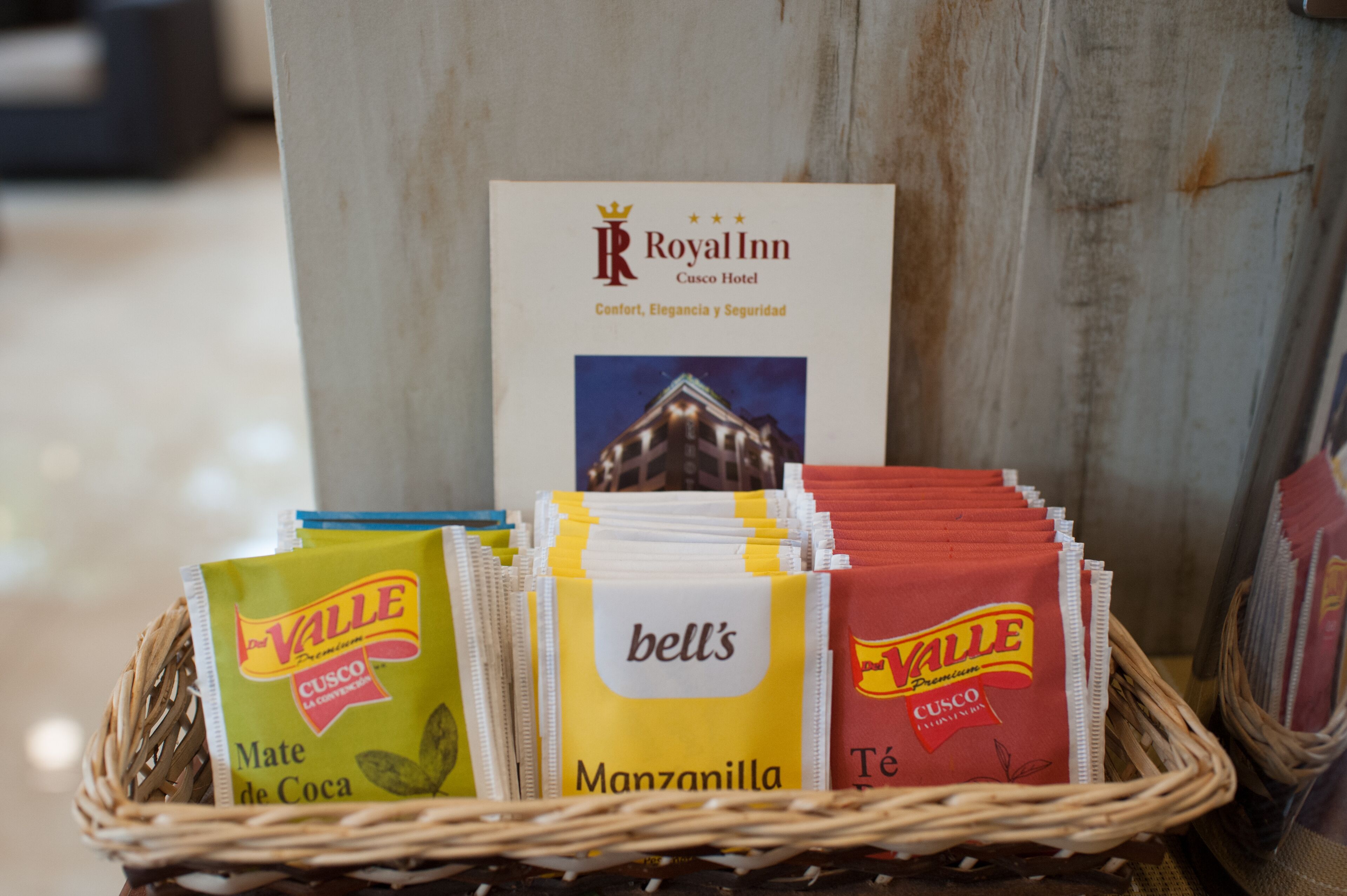 A basket of Valle Mate de Coca and Manzanilla coffee packets, a Royal Inn Cusco Hotel sign, and a wicker basket.