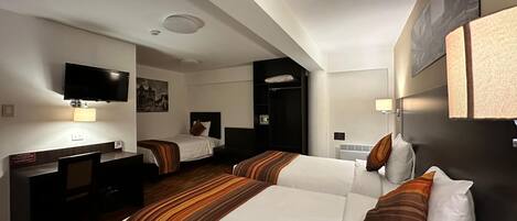 Una camera d'albergo con due letti, una scrivania, un televisore e un appendiabiti.