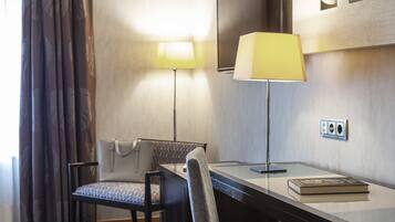 A hotel room with a desk, a chair, a lamp, and a book.