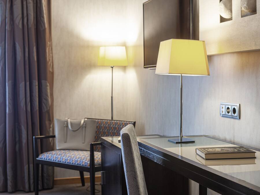 A hotel room with a desk, a chair, a lamp, and a book.