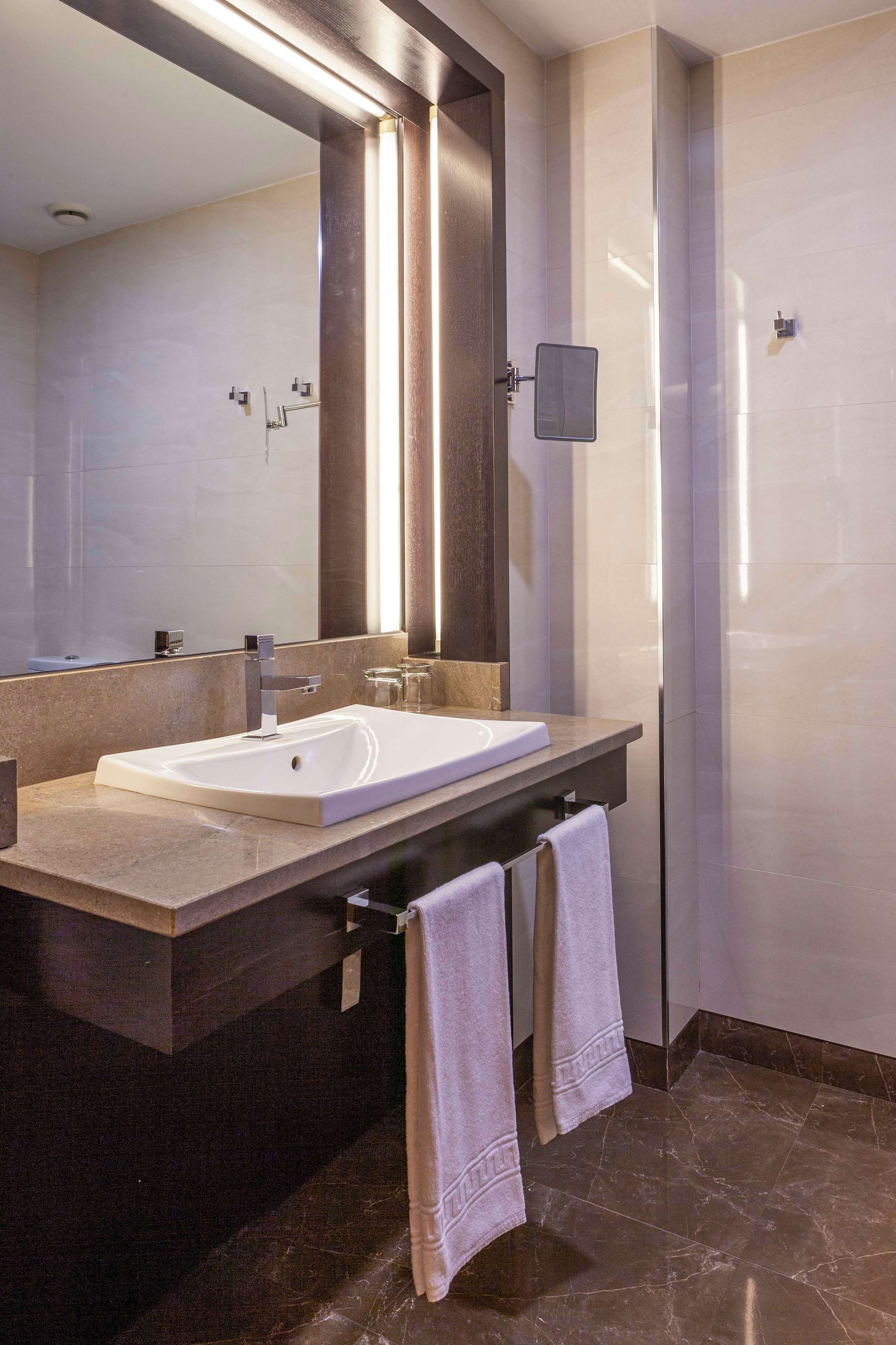 A modern bathroom with a large mirror, a sink, and a shower area.