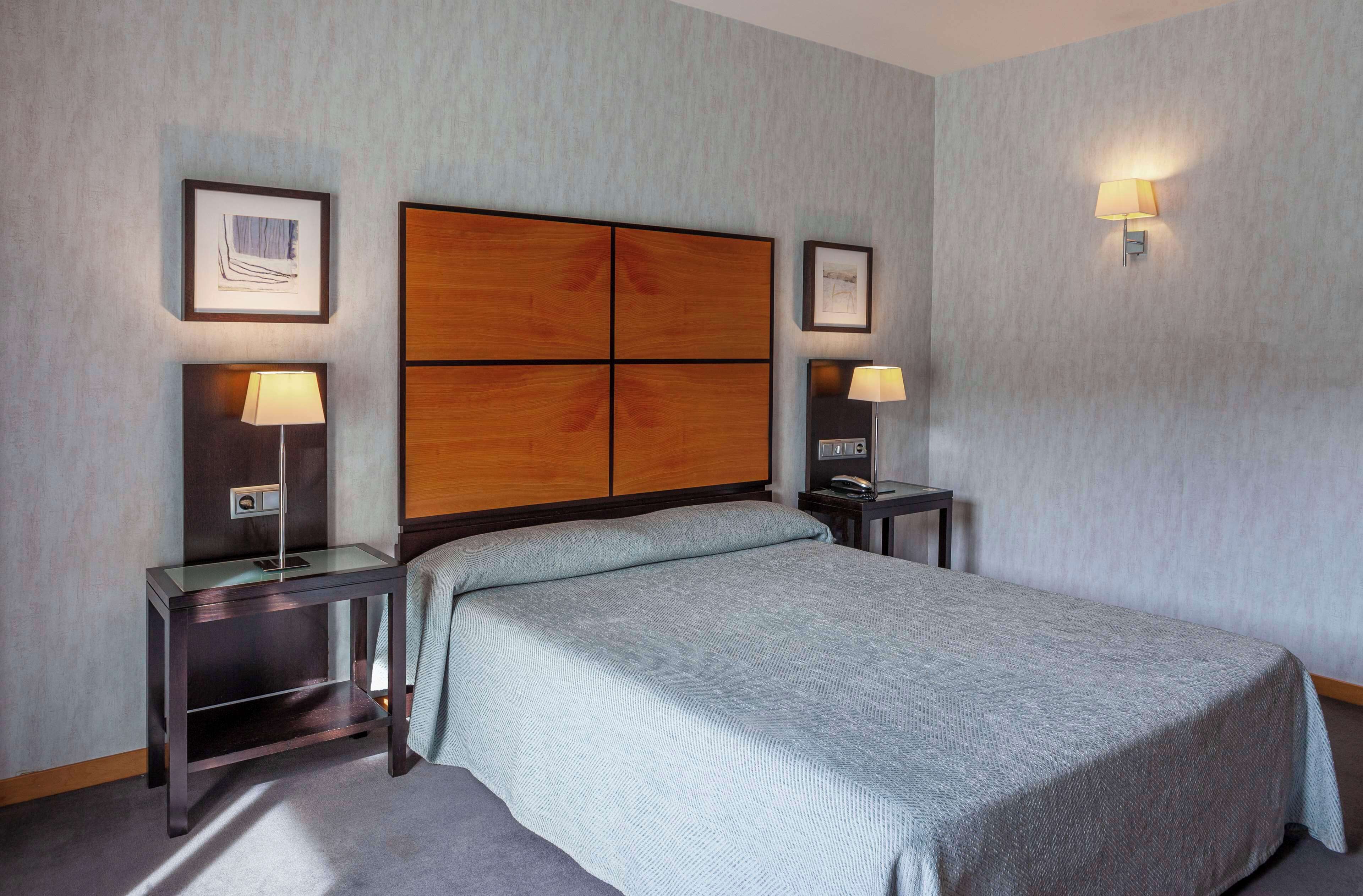 A hotel room with a large bed, two bedside tables with lamps, a wooden headboard, and framed artwork on the walls.
