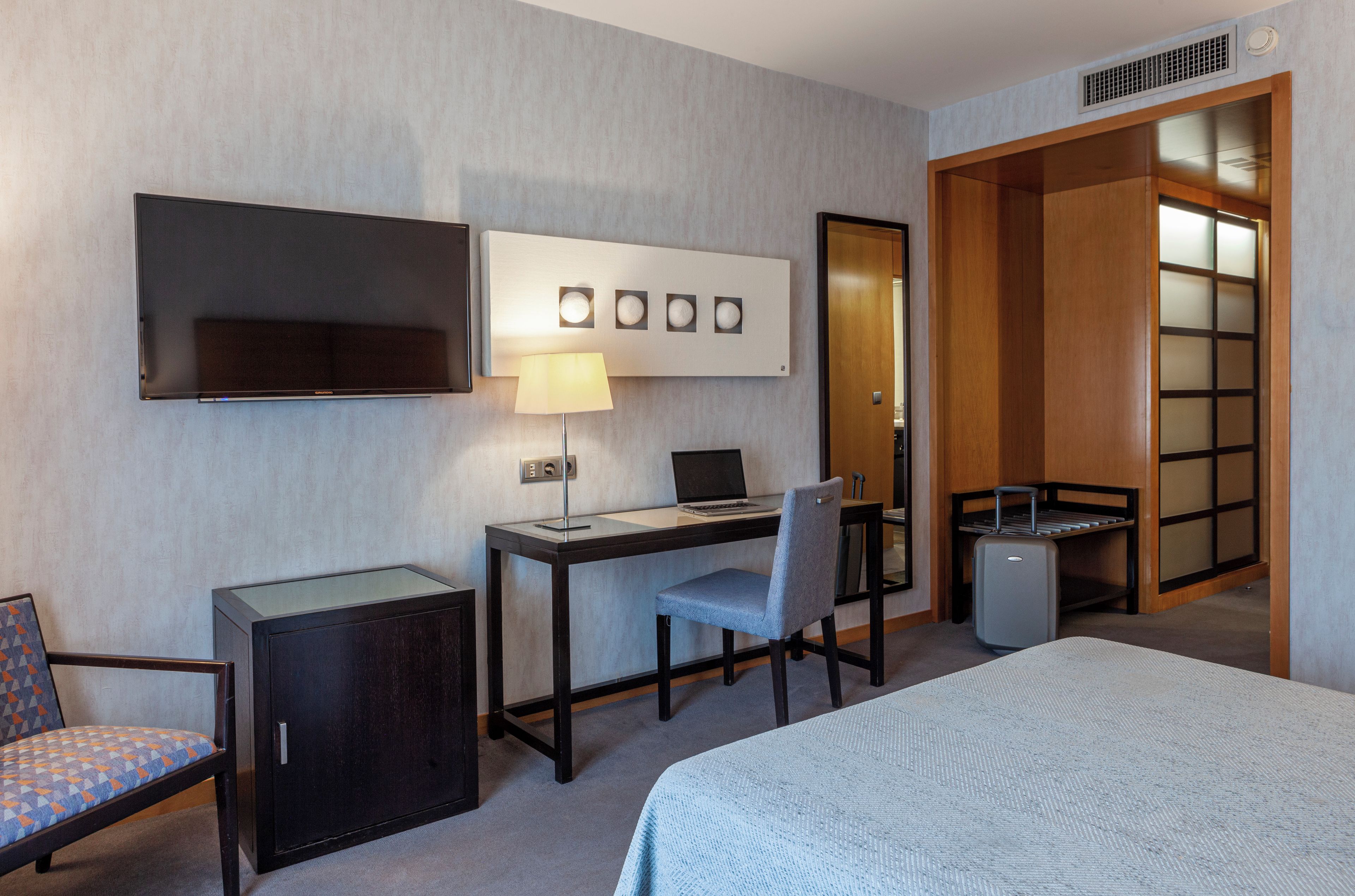 Una habitación de hotel con una cama, un escritorio con una computadora portátil, una silla, un televisor y un armario.
