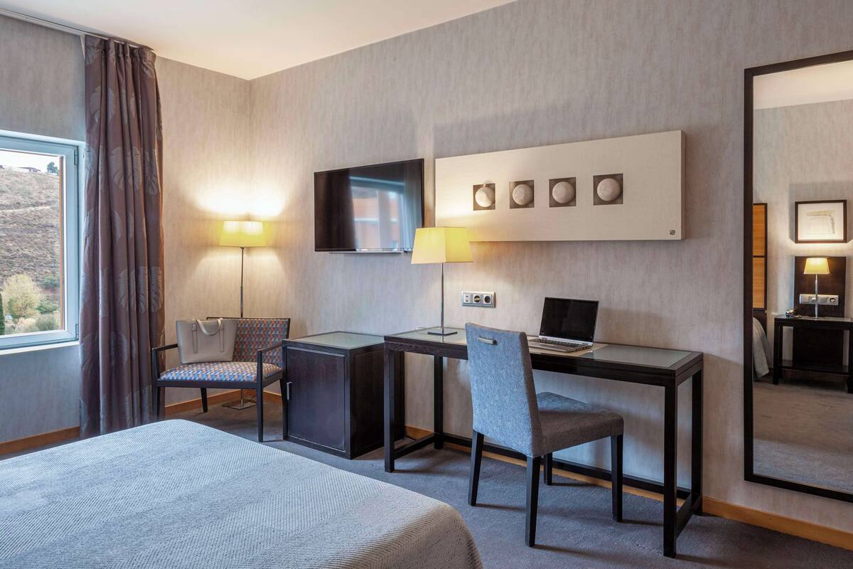 Una habitación de hotel con una cama, un escritorio con silla, un televisor y dos lámparas.