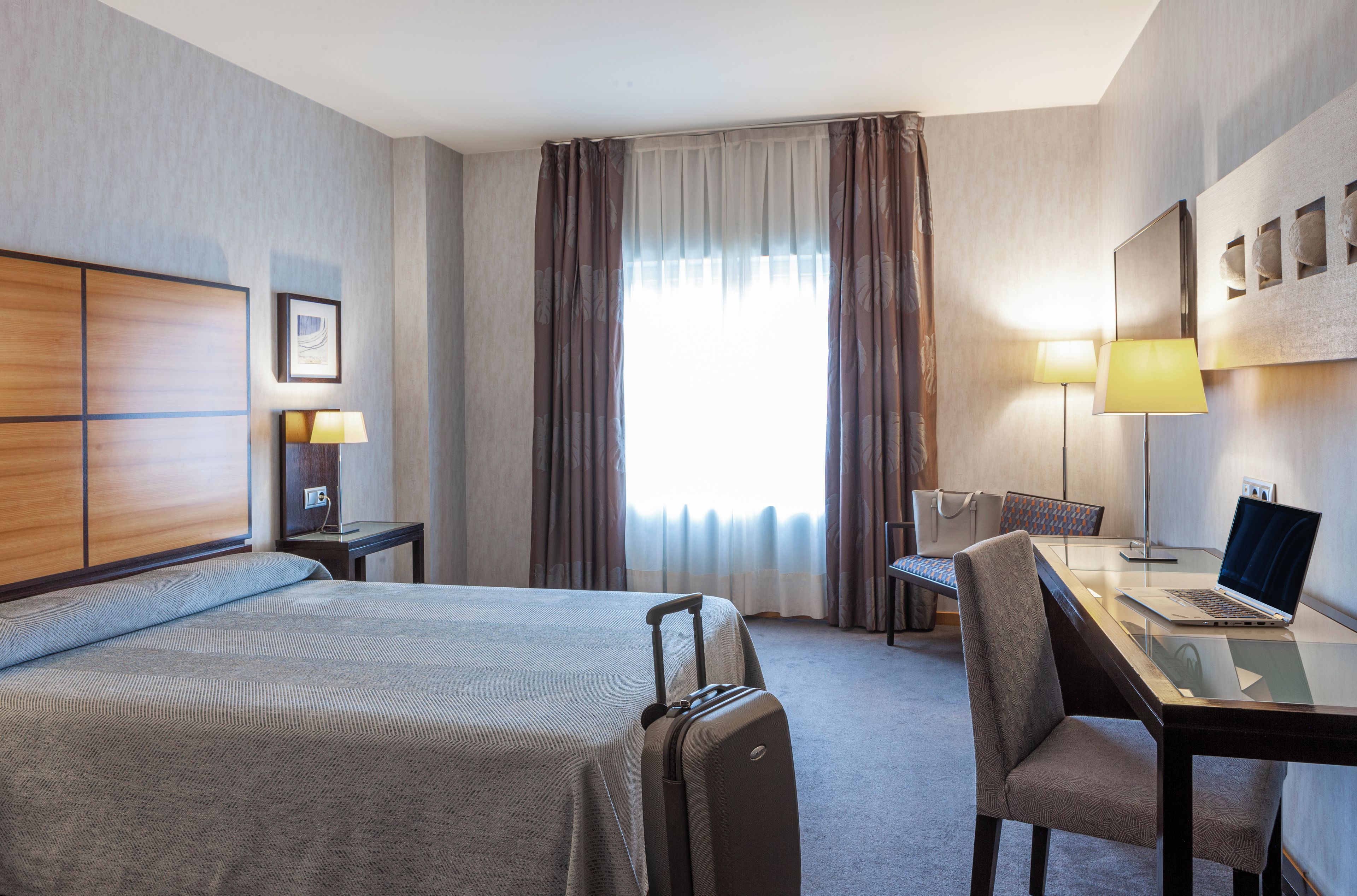 Una habitación de hotel con cama, escritorio, silla y una computadora portátil.