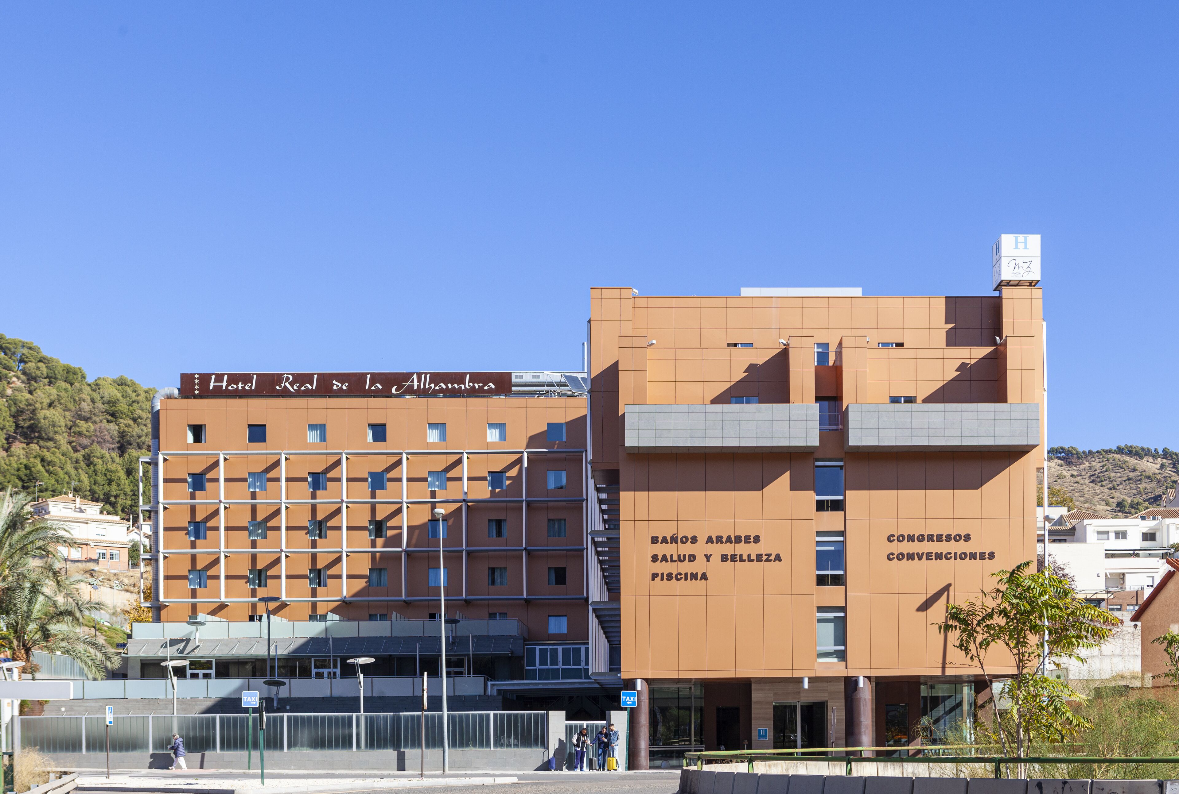 Un hotel con varios pisos, balcones y un letrero que indica servicios como piscina y salas de conferencias.
