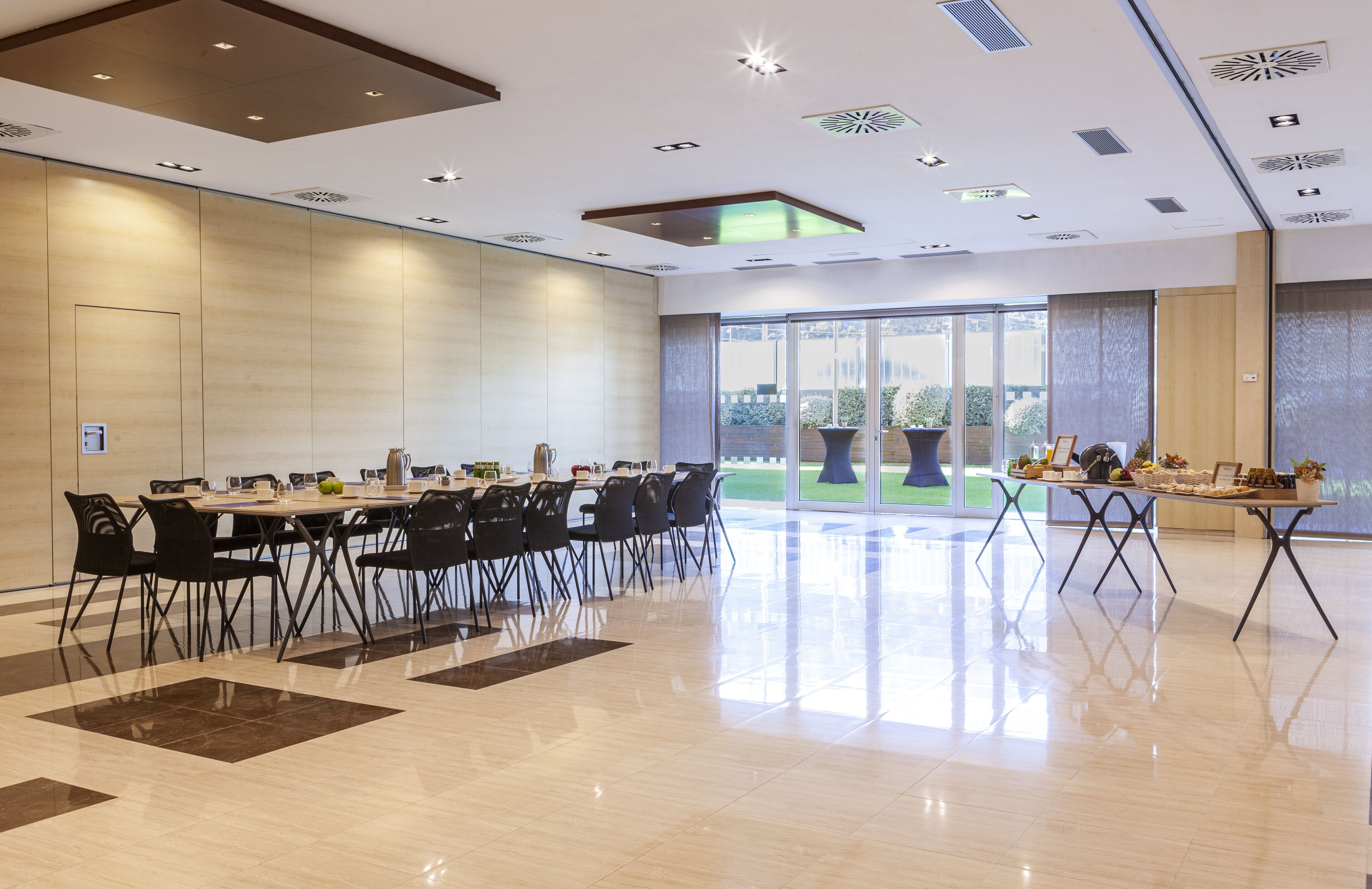 A spacious conference room with a long table, black chairs, and a glass partition.