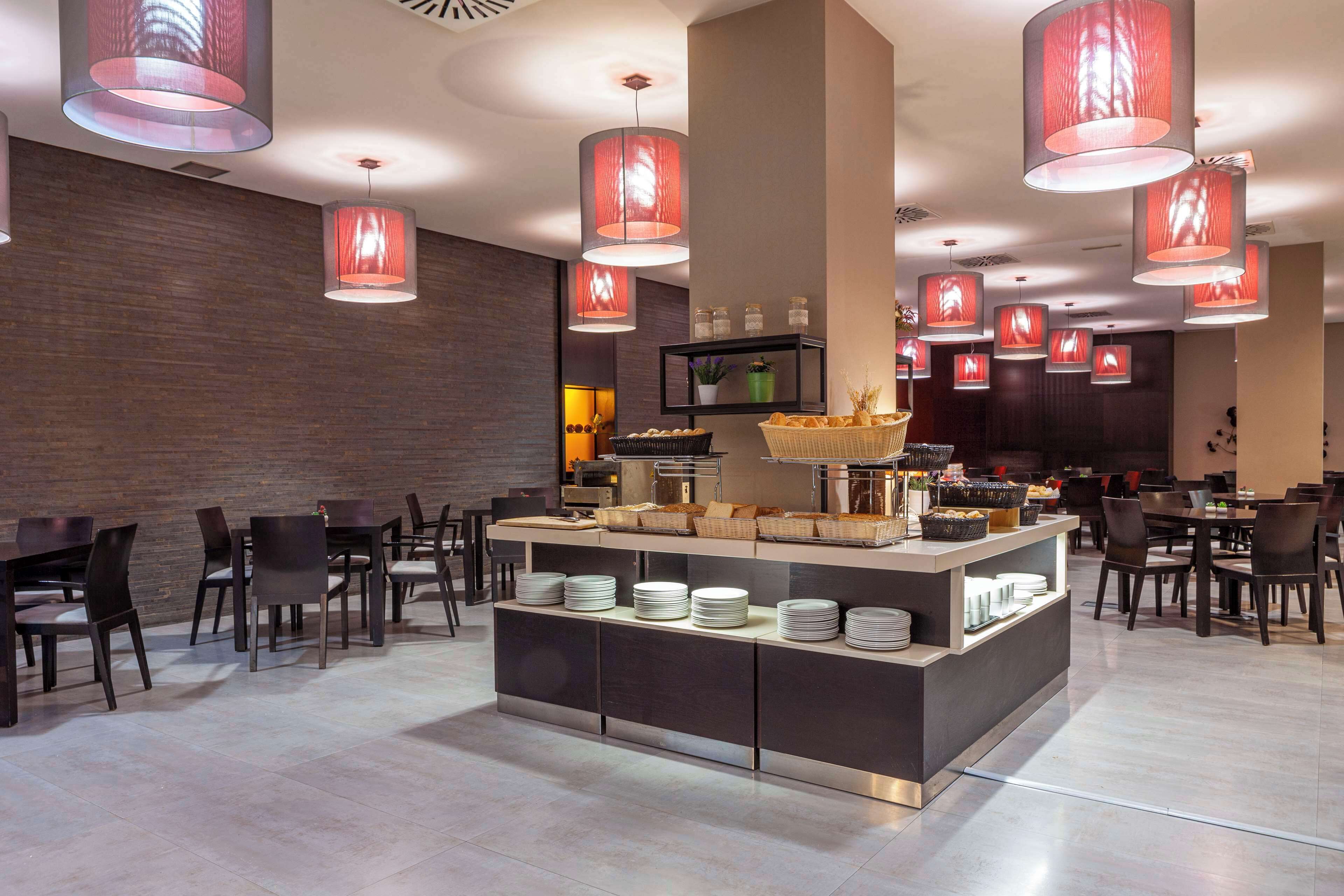 Un restaurant moderne doté d’un buffet central, de nombreuses lampes rouges suspendues et de différents types de mobilier pour créer des espaces de restauration variés.