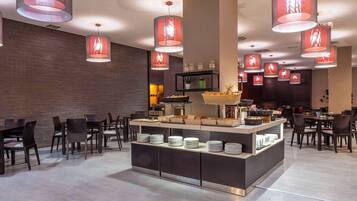 Un restaurant moderne doté d’un buffet central, de nombreuses lampes rouges suspendues et de différents types de mobilier pour créer des espaces de restauration variés.