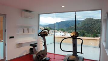 Une salle de sport équipée de deux tapis de course, d’un climatiseur fixé au mur et d’une étagère où sont pliées des serviettes.