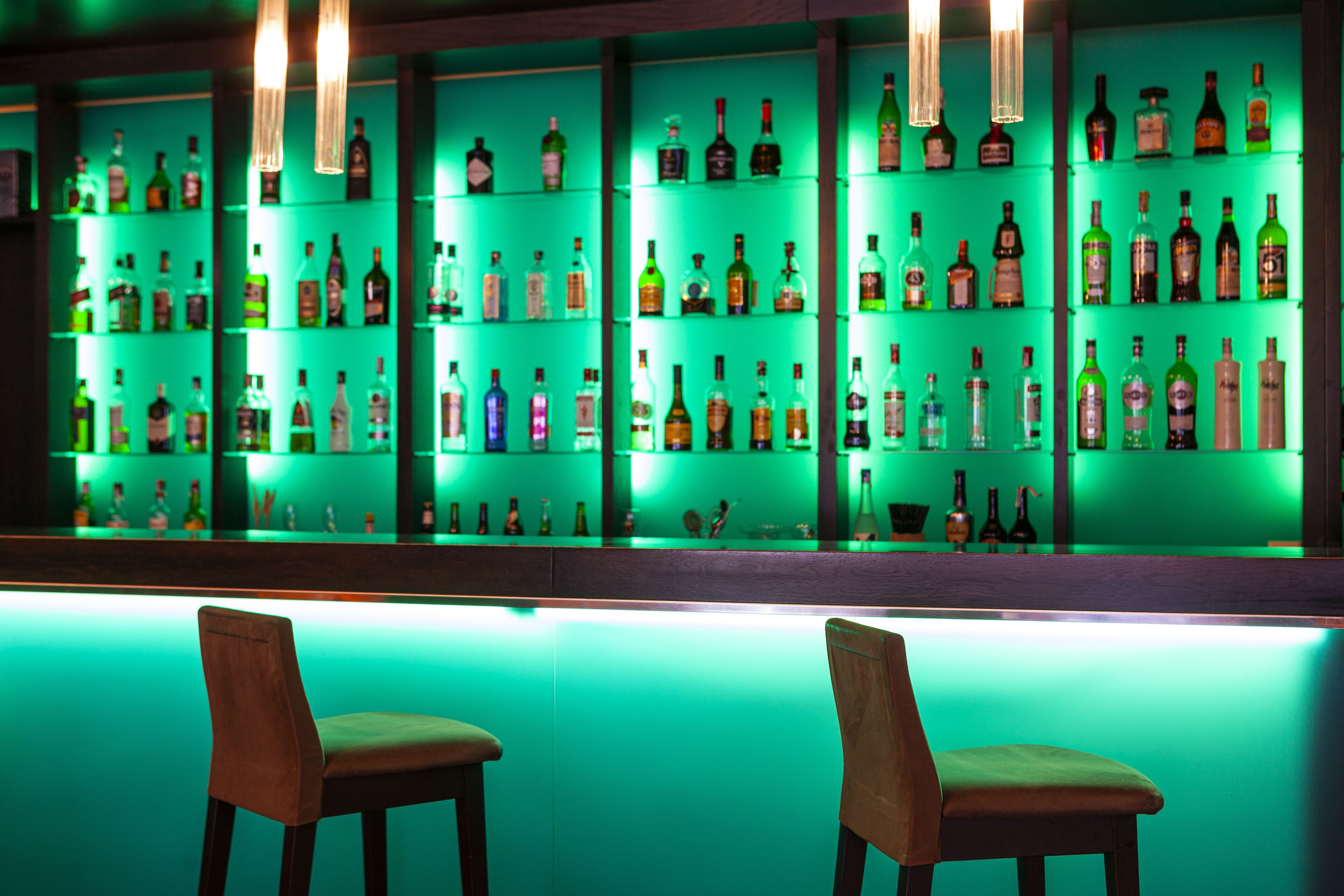 A bar area with multiple shelves of liquor bottles and two wooden chairs.