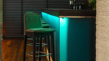 Zona de bar con taburetes color turquesa y una barra, con iluminación colgante y una pared oscura con líneas horizontales.