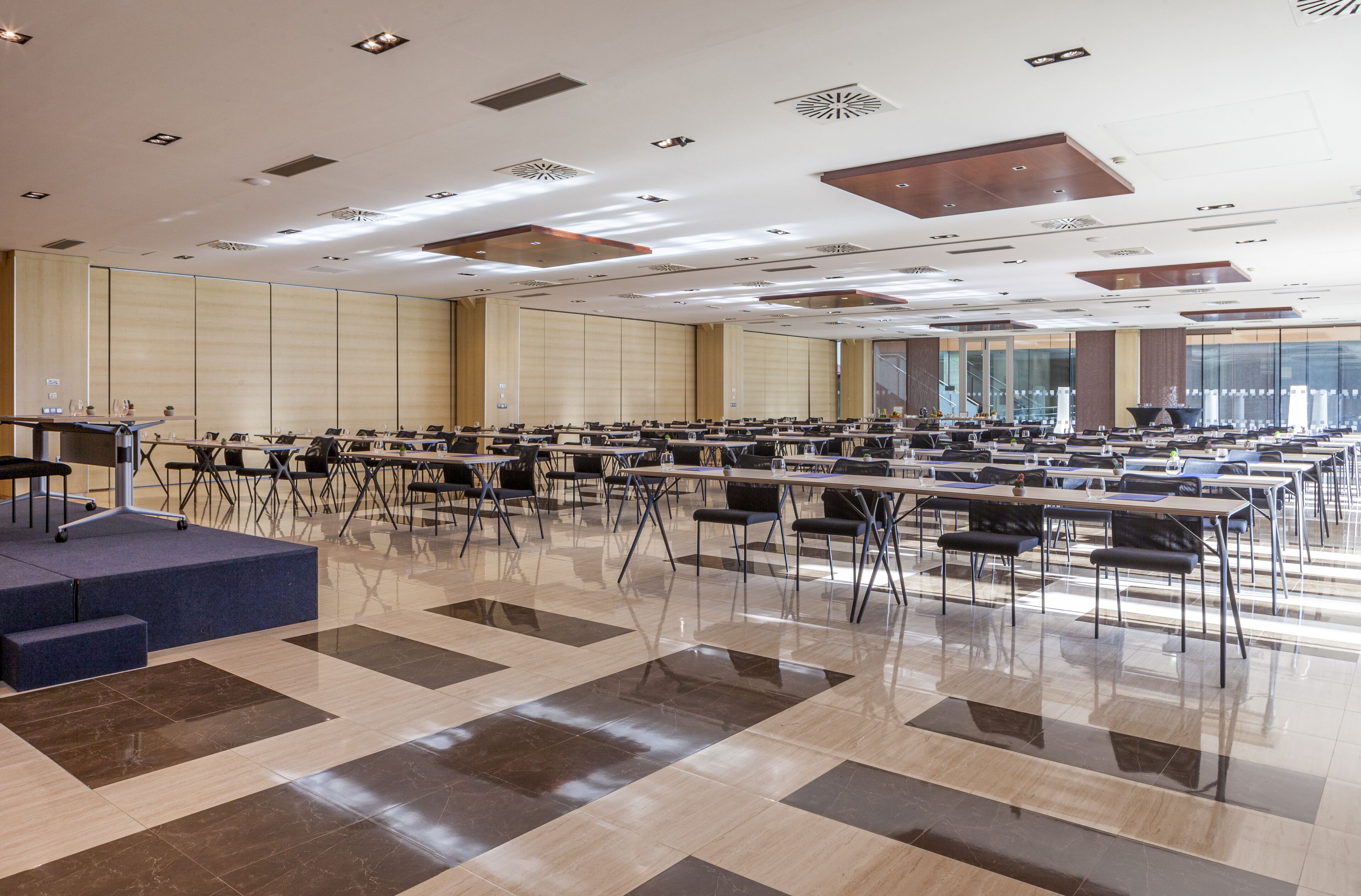 A large conference room with multiple tables and chairs, a stage, and a polished floor.