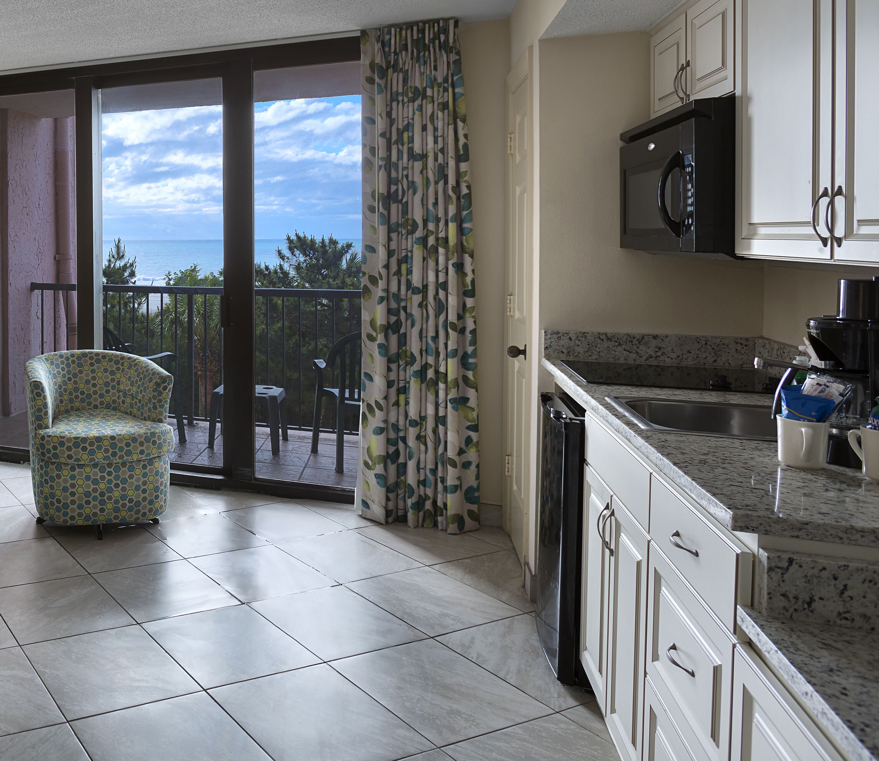 Una cocina con vista al mar, una zona de comedor con una silla y una puerta corrediza de vidrio.