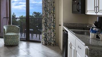 A kitchen with a view of the sea, a dining area with a chair, and a sliding glass door.
