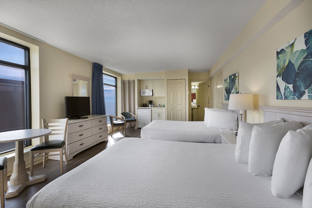 A hotel room with a bed, a desk, a chair, a television, and a kitchenette.