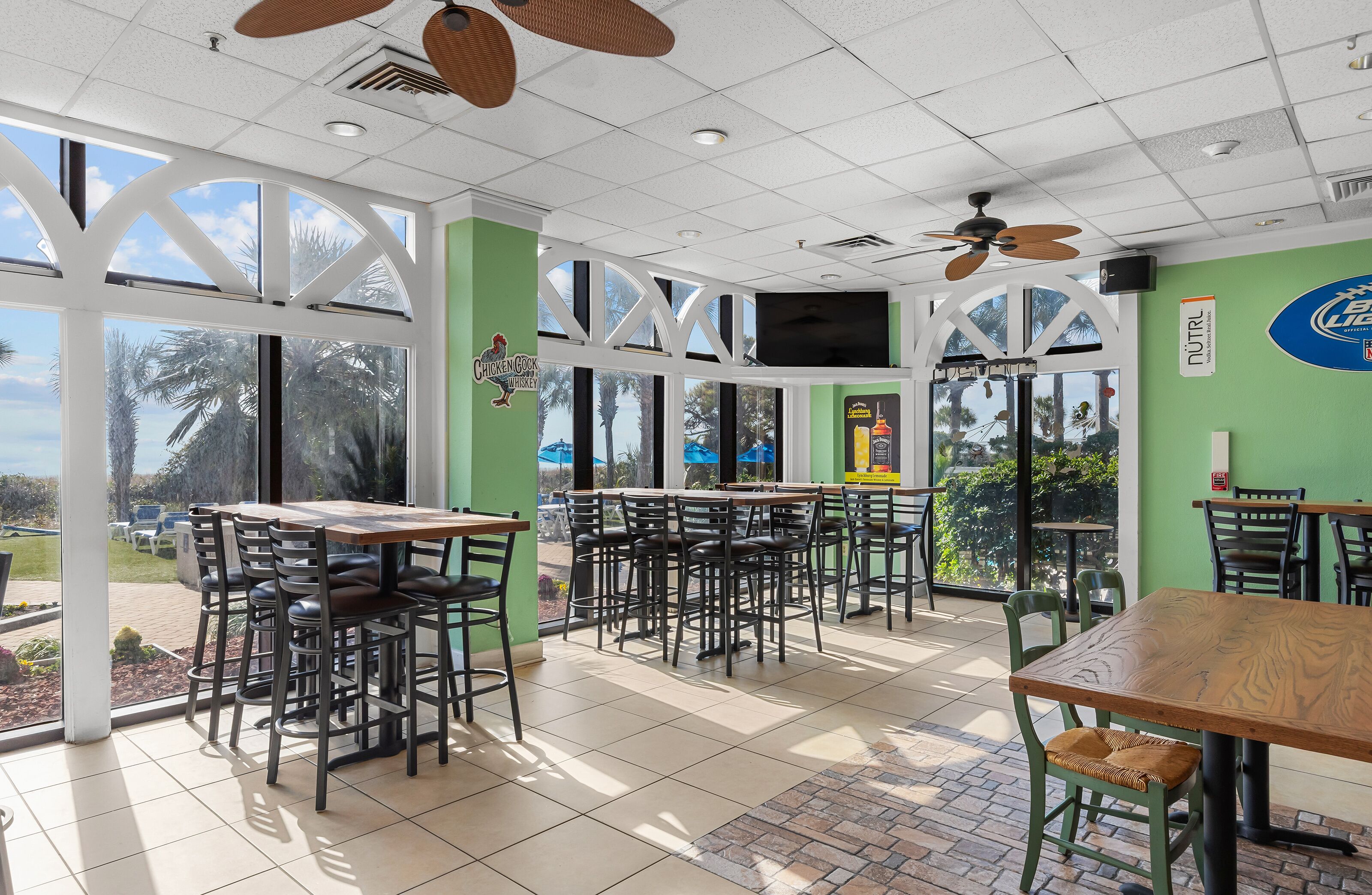 Un restaurante con terraza, grandes ventanales y vistas a palmeras.