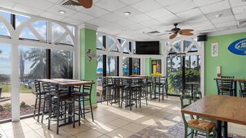 Un restaurante con terraza, grandes ventanales y vistas a palmeras.