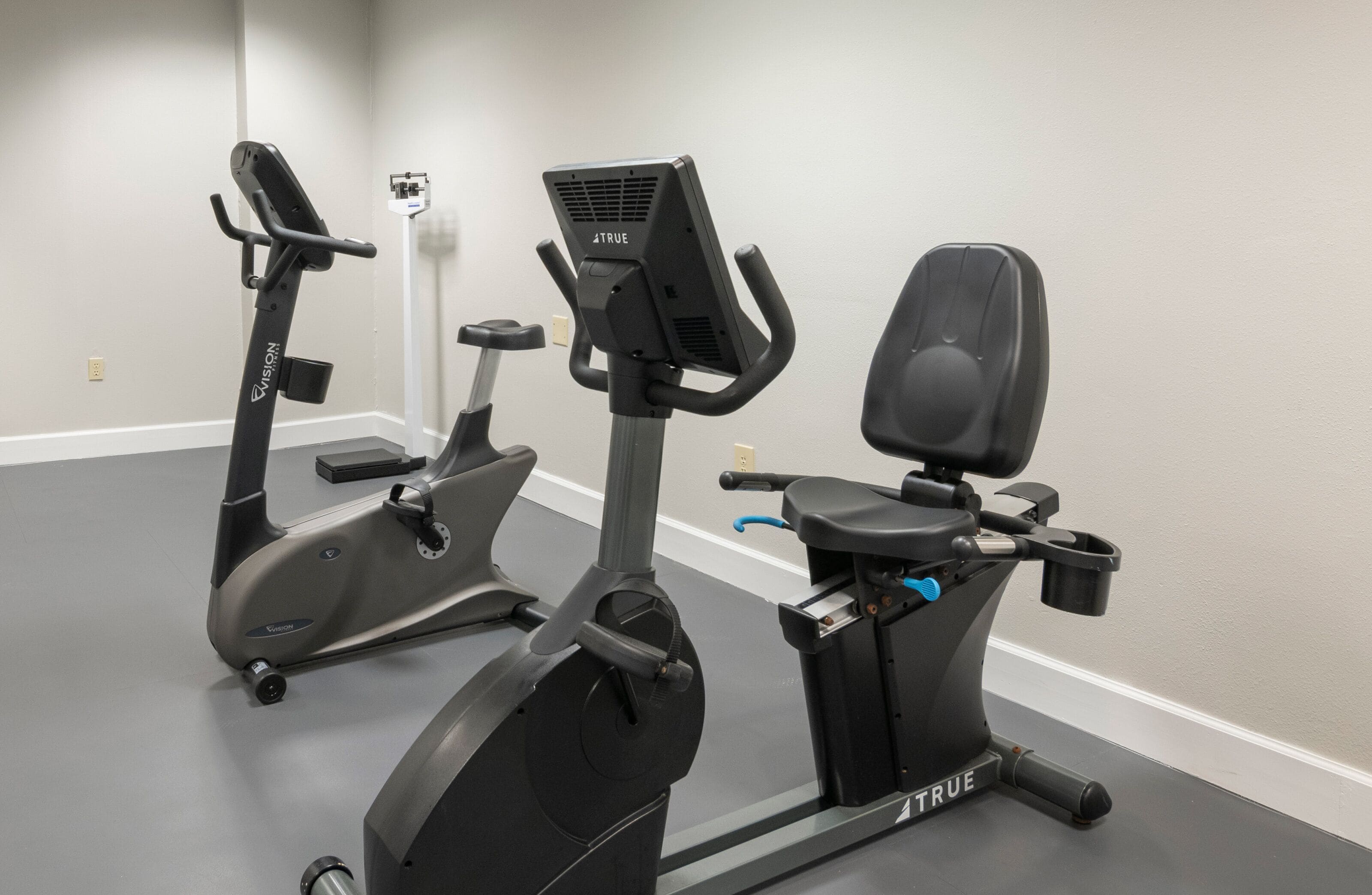 Two exercise bikes in a gym with a gray floor and white walls.