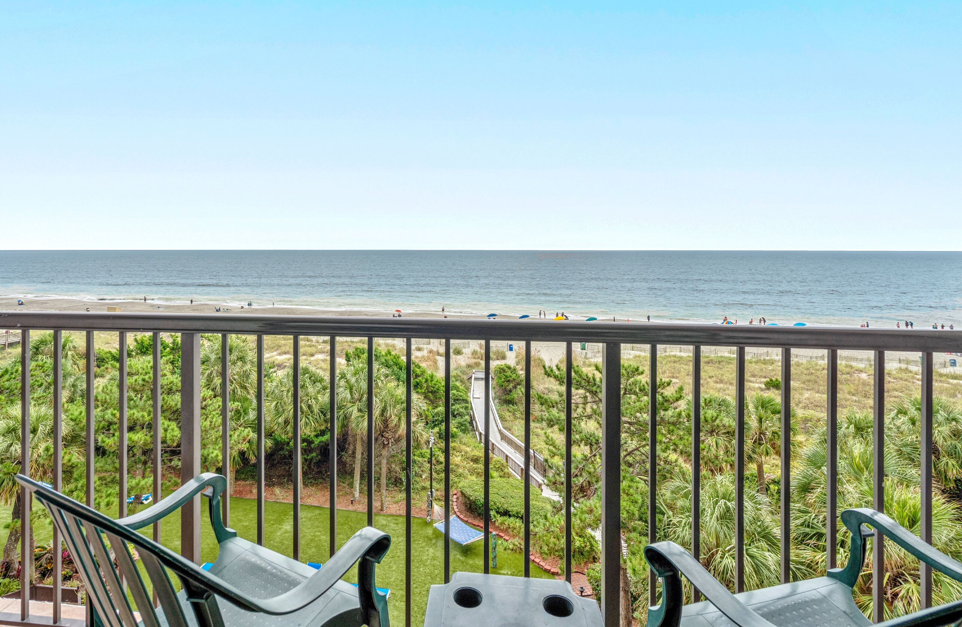 A balcony with a view of the beach and a garden.