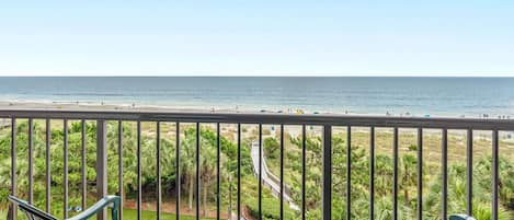 A balcony with a view of the beach and a garden.