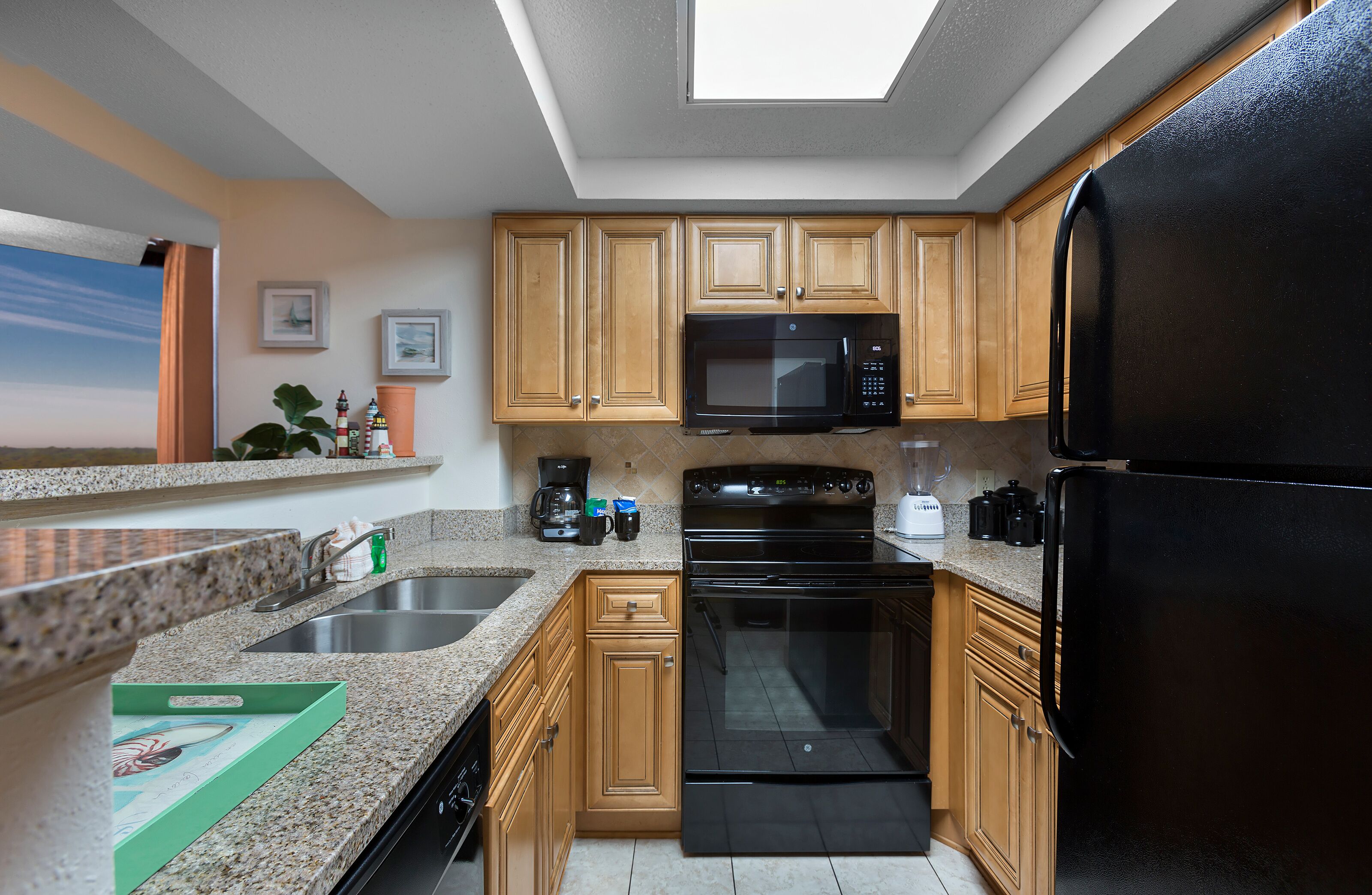 Una cocina con encimeras de granito, armarios de madera, un refrigerador negro, un microondas, una estufa y un lavavajillas.