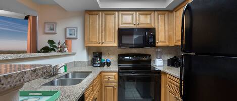 Una cocina con encimeras de granito, armarios de madera, un refrigerador negro, un microondas, una estufa y un lavavajillas.