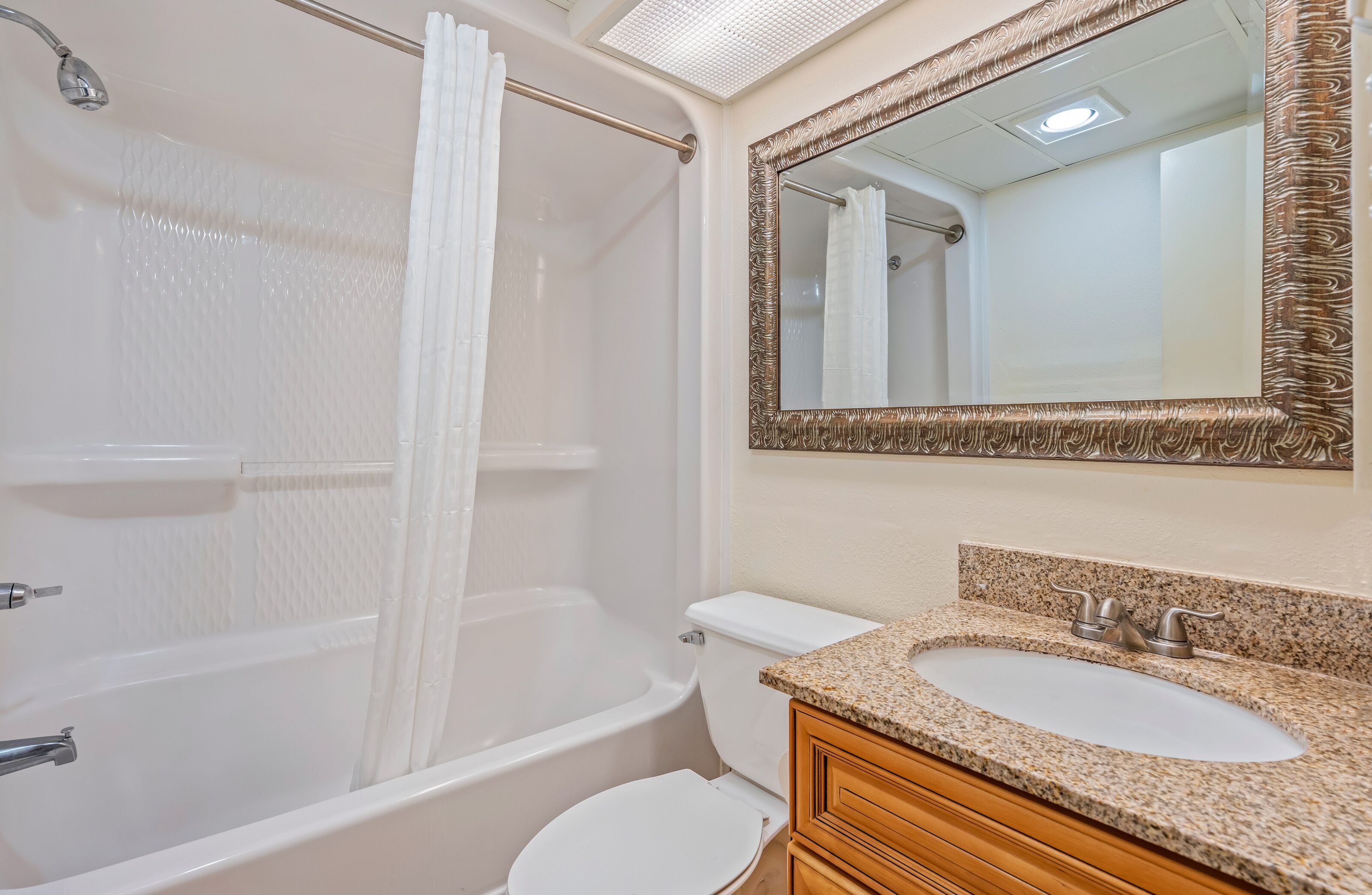 Une salle de bain équipée d’une baignoire, de toilettes, d’un lavabo et d’un miroir avec un cadre décoratif.