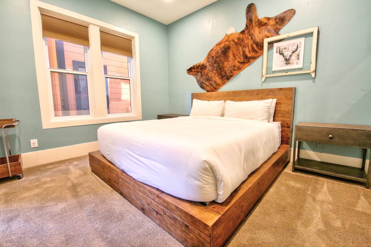 Ein Schlafzimmer mit einem großen Bett, einem hölzernen Kopfteil, einem Fenster und einer an der Wand befestigten Skulptur eines Tierkopfes.