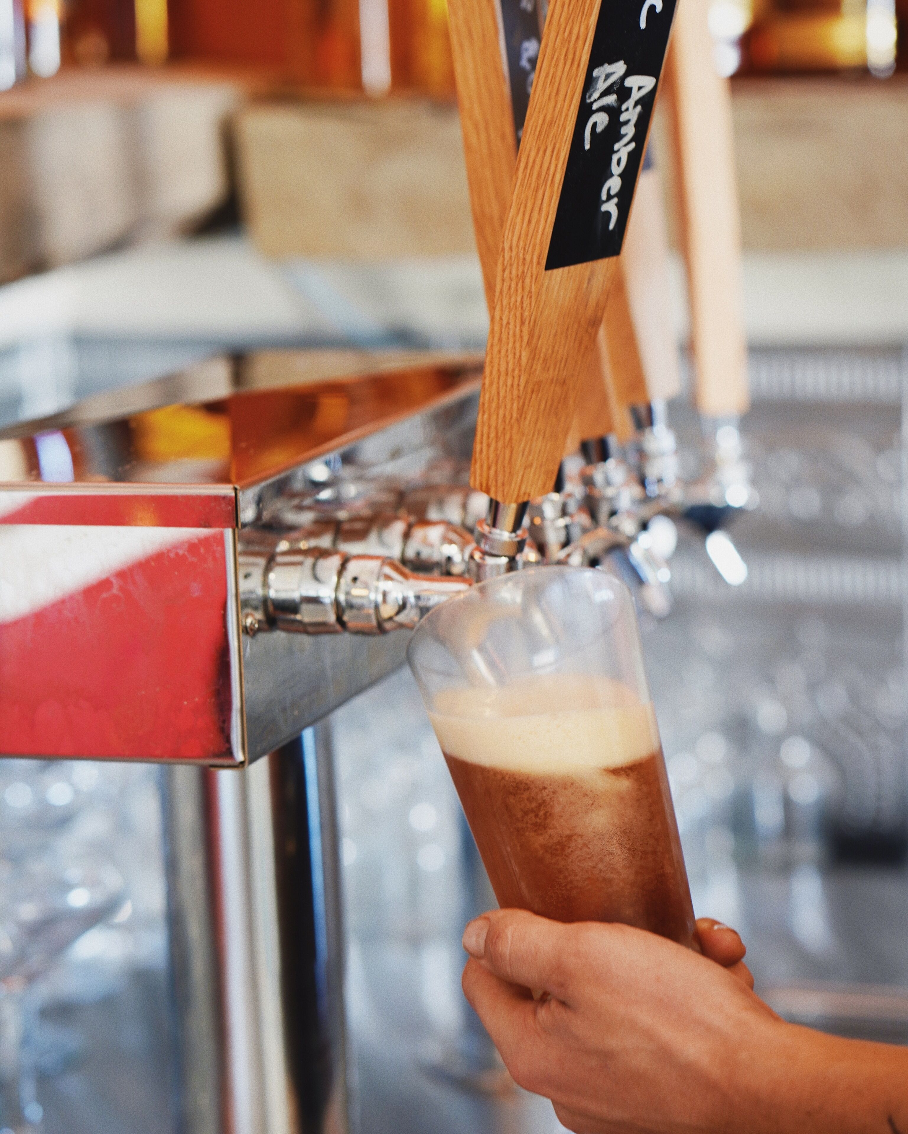 Une main tenant un verre dans lequel on verse de la bière ambrée, provenant d’une tireuse portant l’inscription « Amber Ale ».
