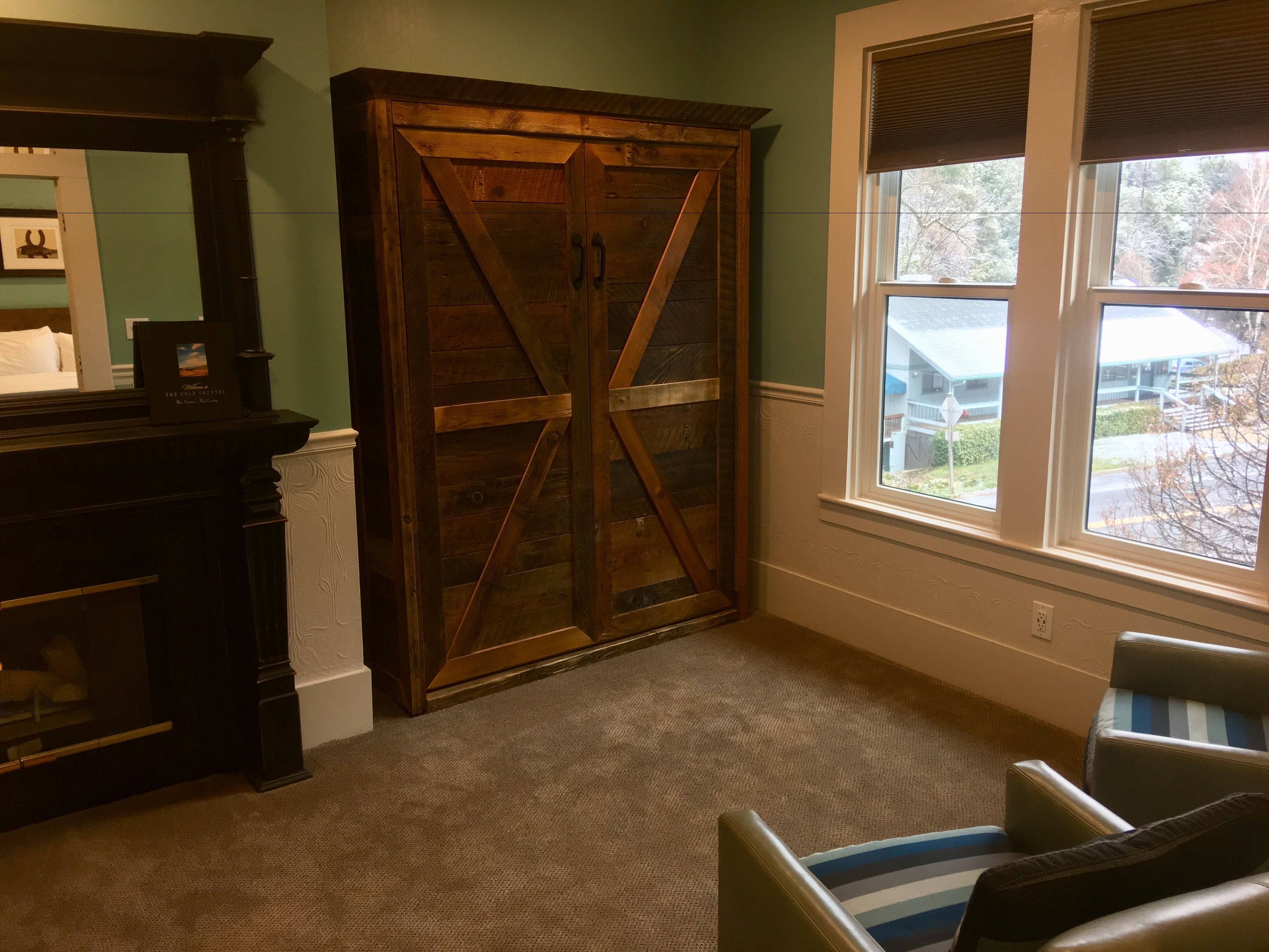 A room with a large wooden wardrobe, a fireplace, a window with blinds, and a striped chair.