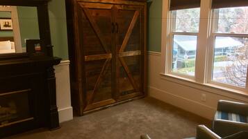 A room with a large wooden wardrobe, a fireplace, a window with blinds, and a striped chair.