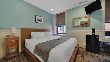 A hotel room with a bed, a nightstand, a mirror, a TV, and a window with blinds.