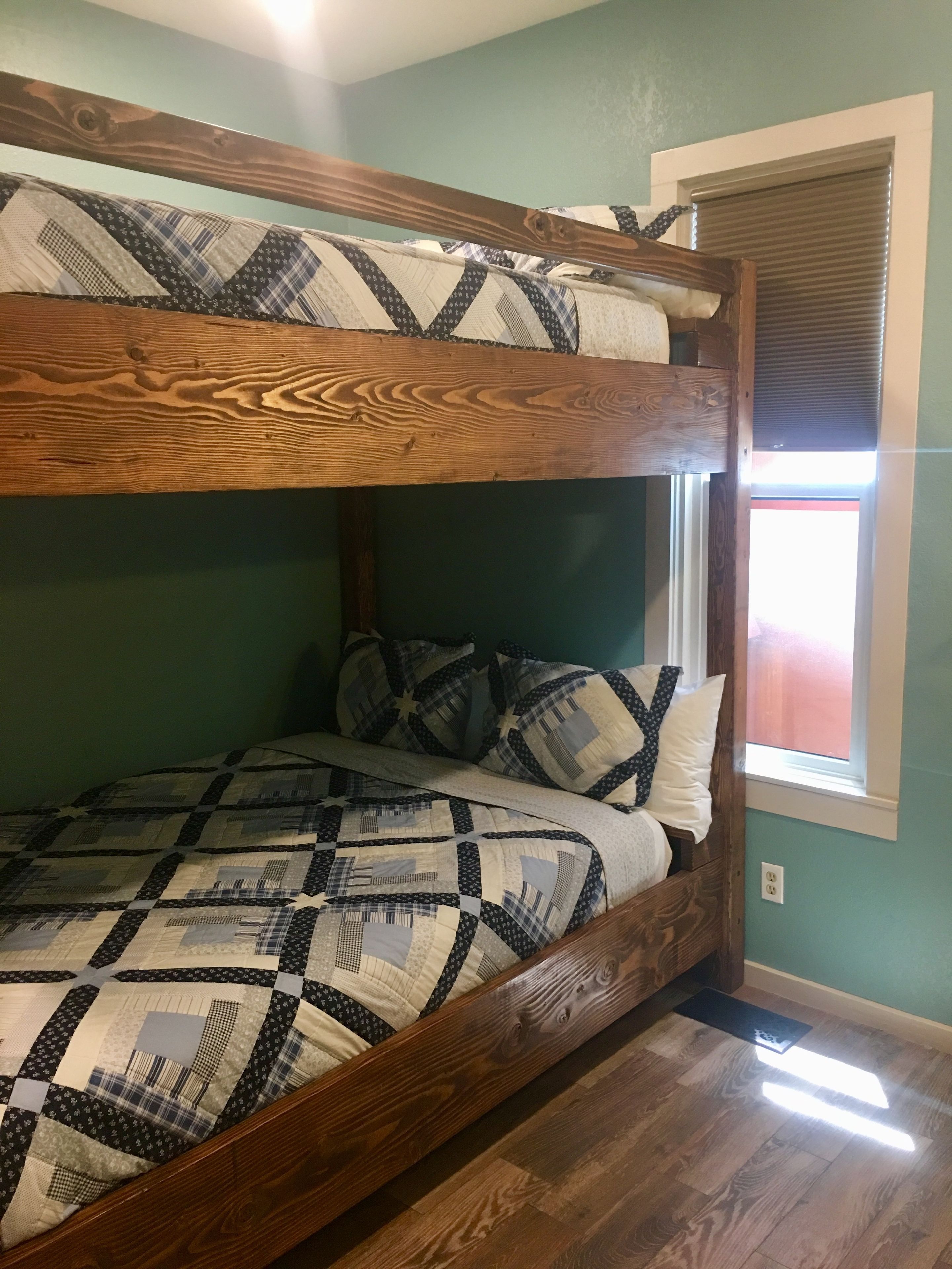 A bunk bed with a patterned bedspread and pillows, wooden headboard, and a window with blinds.