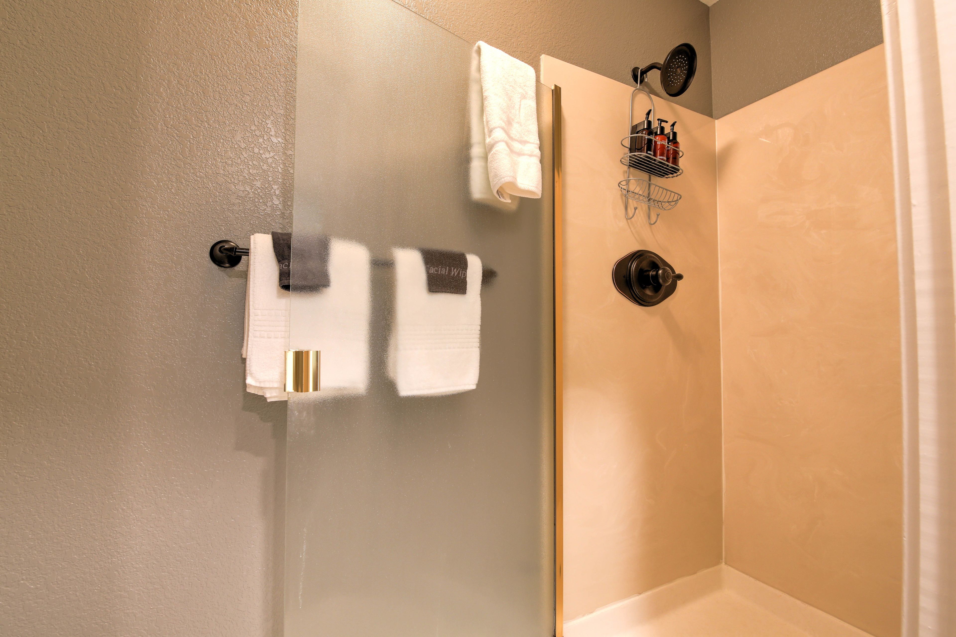 A bathroom with a glass shower door, a towel rack with multiple towels, and a showerhead.