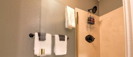 A bathroom with a glass shower door, a towel rack with multiple towels, and a showerhead.