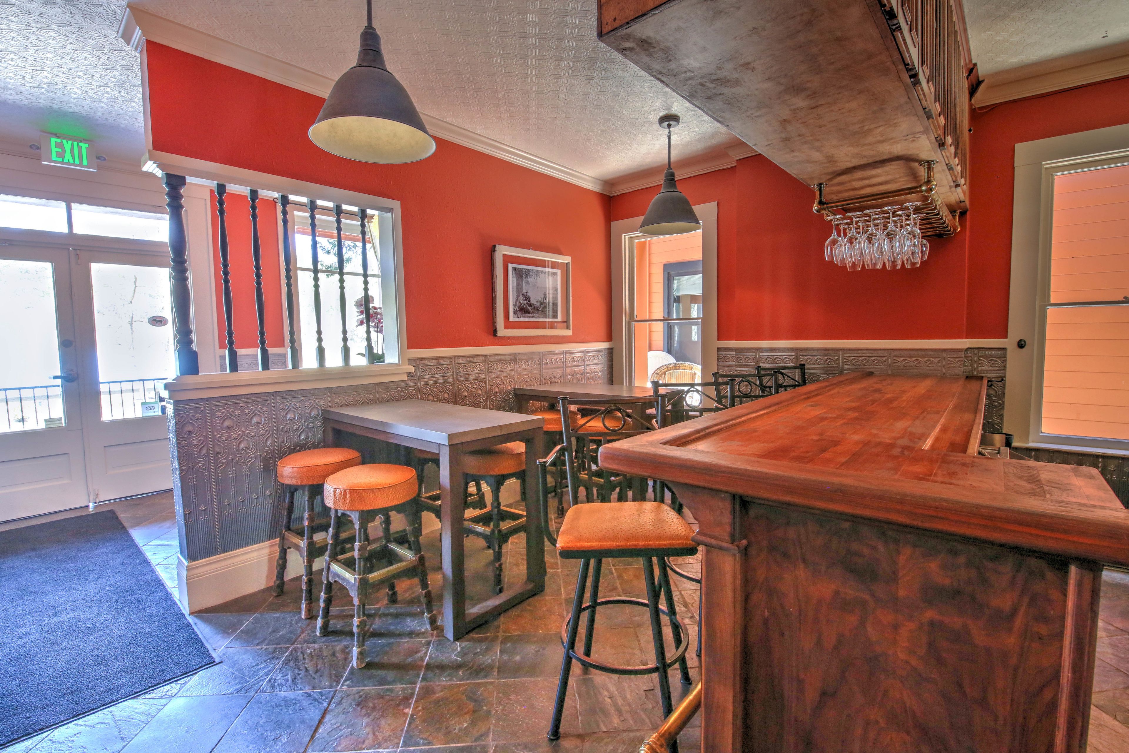 A bar area with stools, a wooden counter, and hanging light fixtures.