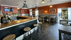 A bar area with a wooden counter, stools, and pendant lighting. There are framed pictures on the walls and a refrigerator stocked with beverages. - The Groveland Hotel (Groveland)