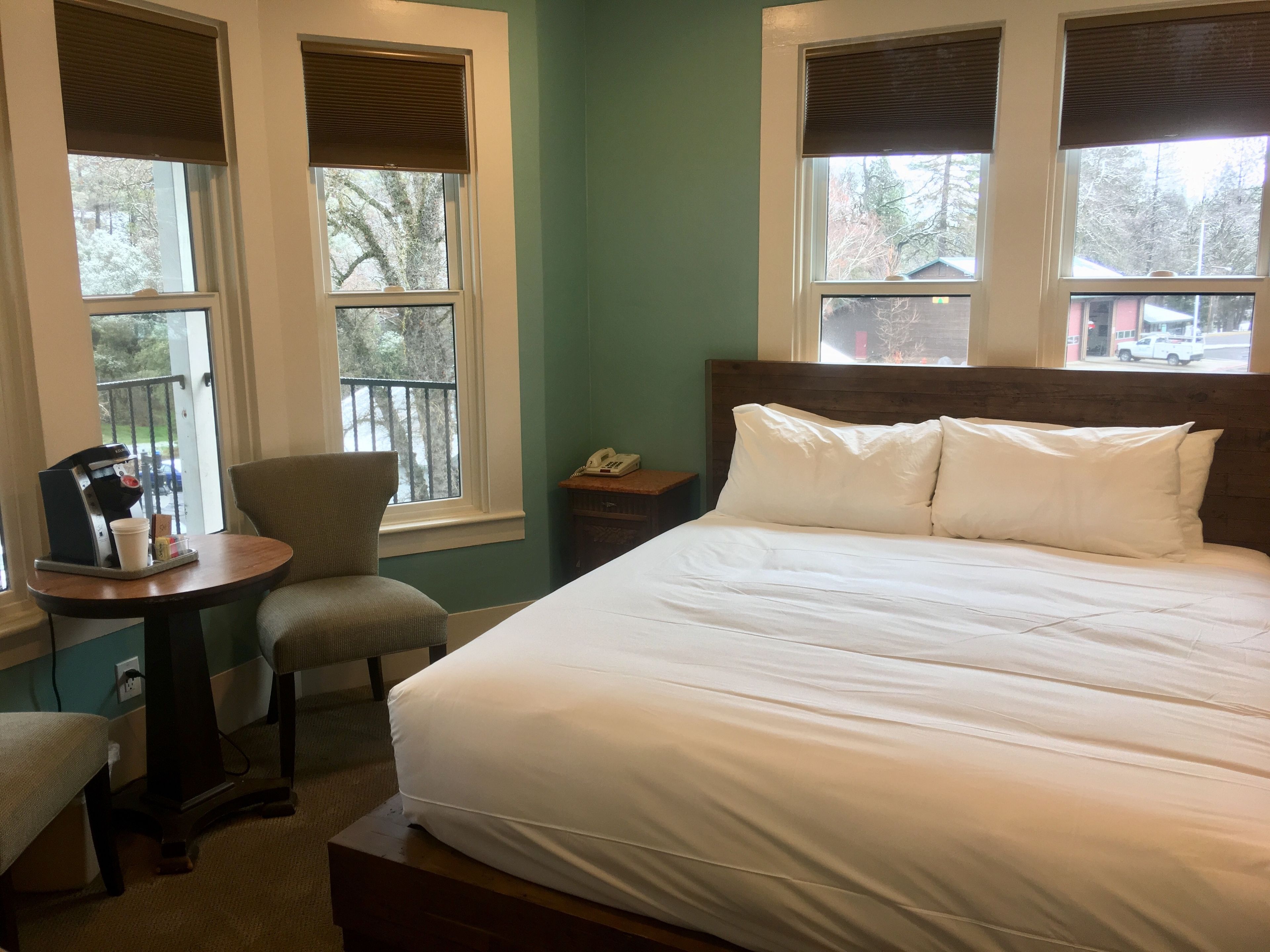 A hotel room with a bed, a chair, a small table with a coffee machine, and a phone on a nightstand.